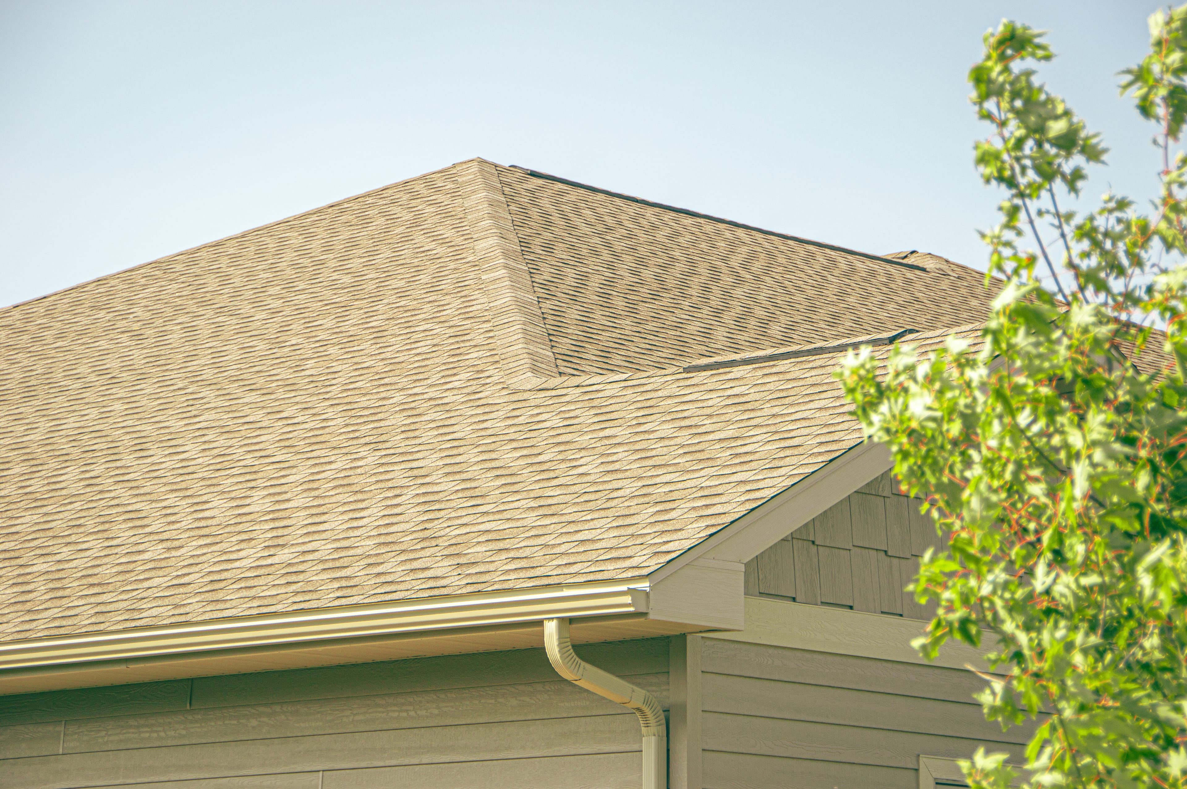 A finished architectural-shingle hip roof with new seamless gutter and a shake-look gable