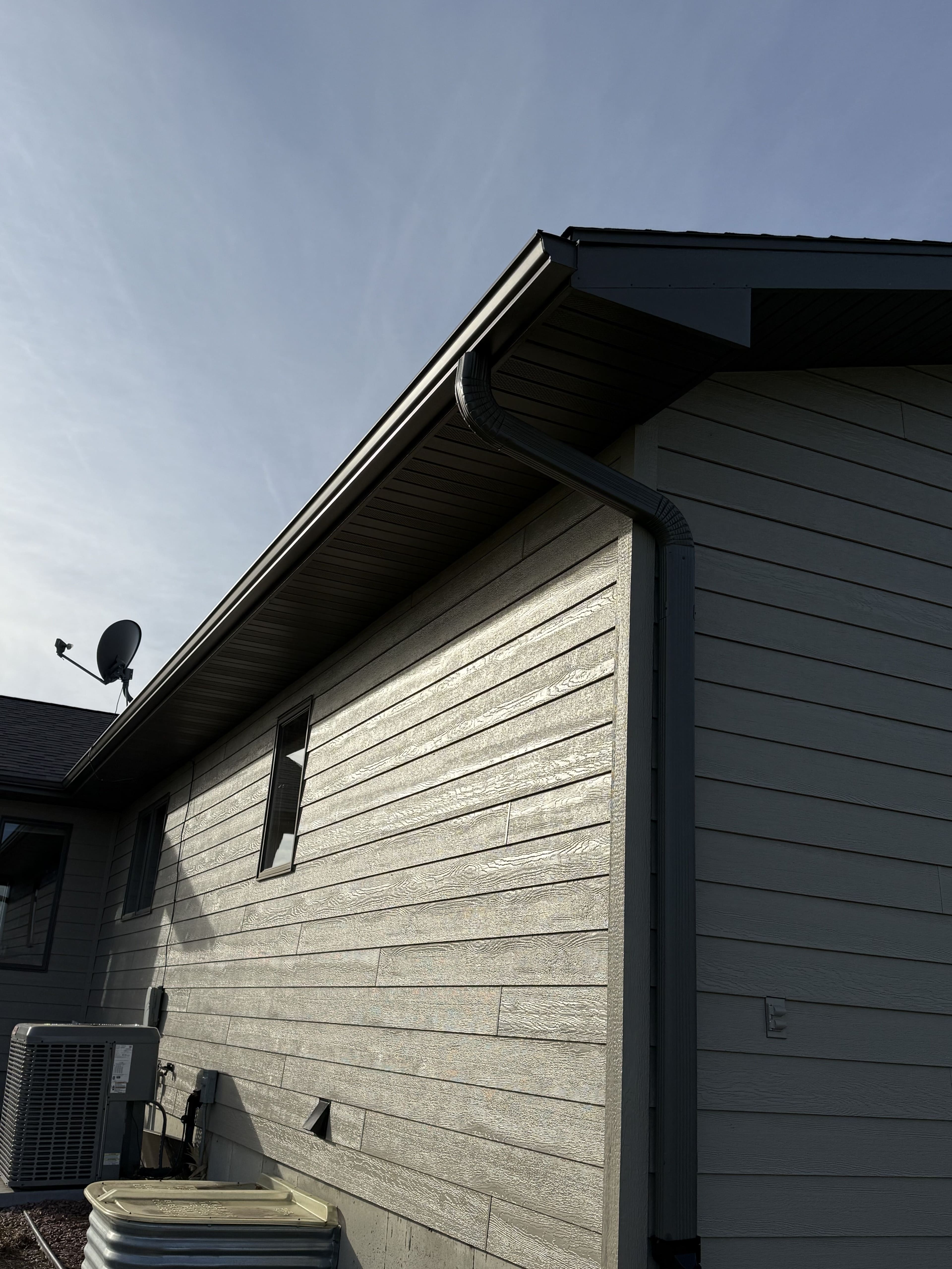 An up-shot into a dark soffit, fascia and gutter with the downspout turning down over two-tone lap siding