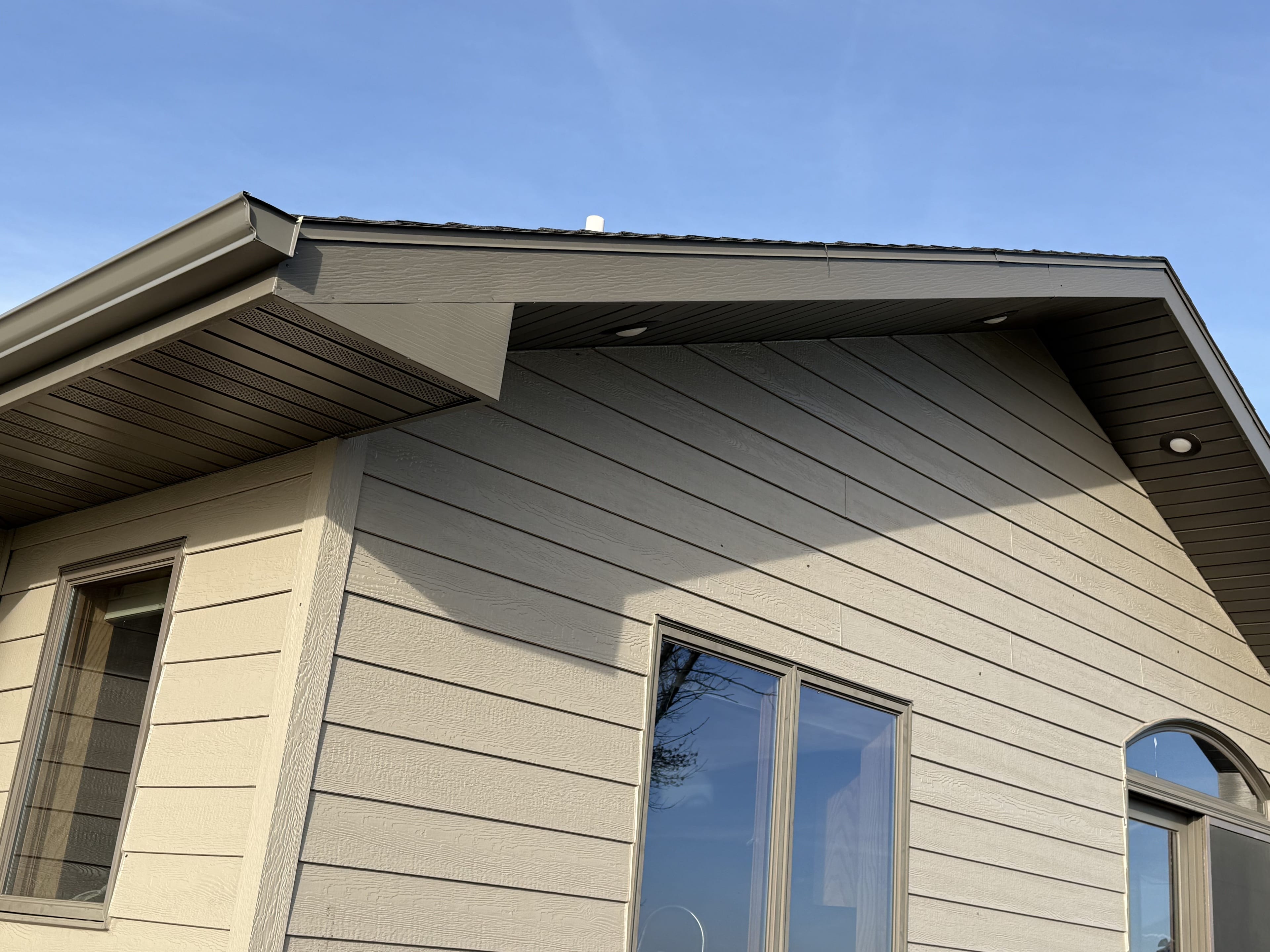A tan lap-siding gable with brown soffit and a new gutter run along the eave, windows below and a clear sky