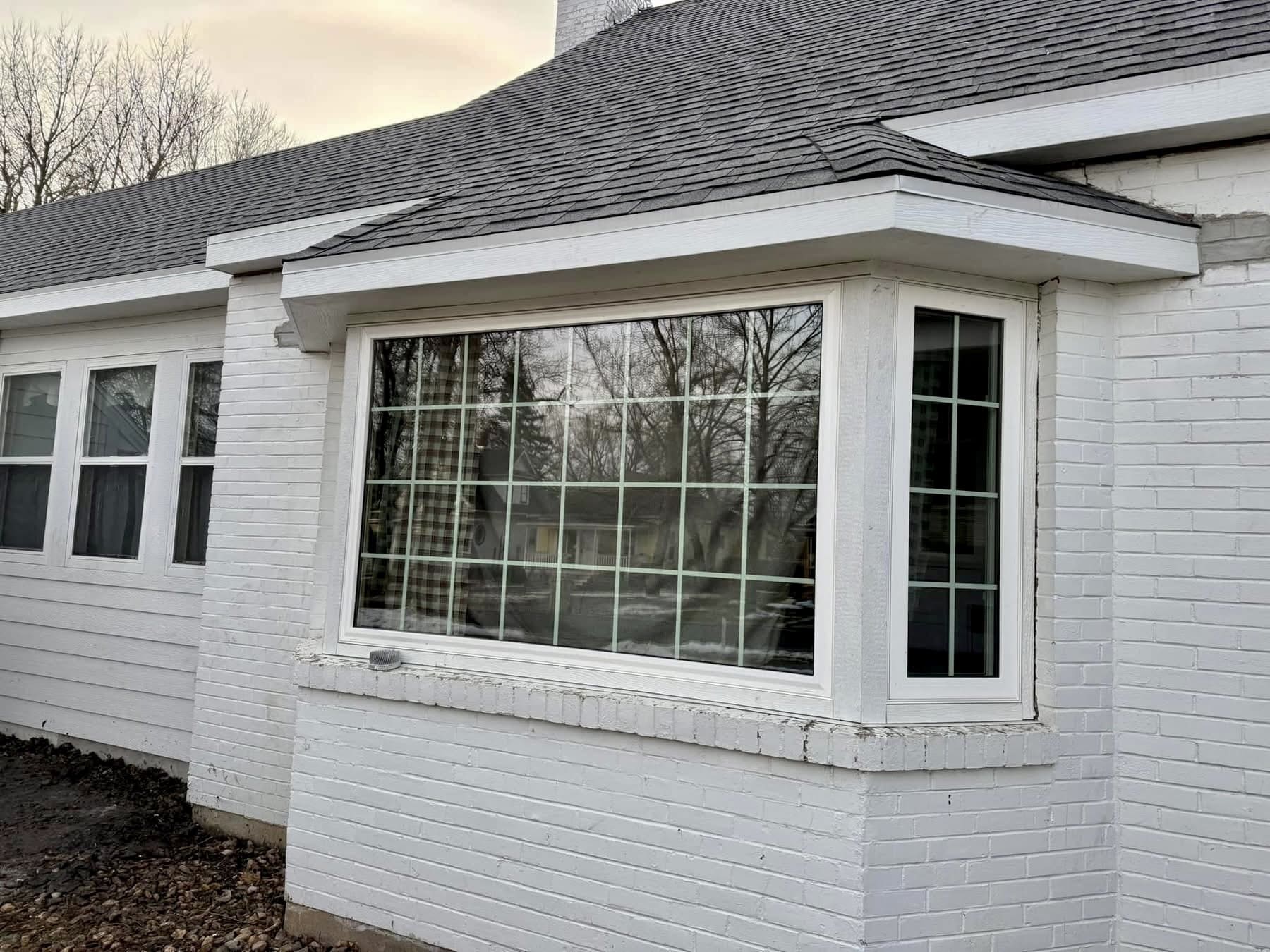 A new bay window installed on a white brick ranch home, with a smaller divided-lite window set into the return beside it