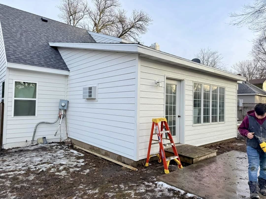 A sunroom addition finished with new white vinyl siding, a glass door and large new windows across the wall