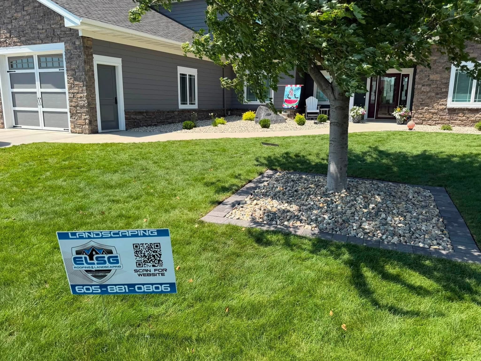 Fresh sod, a paver-edged rock bed set around the tree, river rock along the foundation, and our own yard sign in the grass.